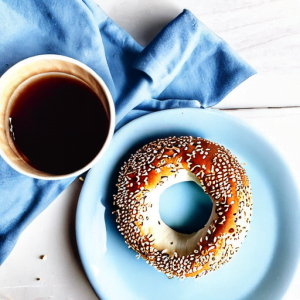 sesame seed bagel with hole in the middle on blue plate with coffee cup